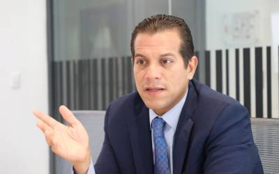 Businessman in a navy suit gestures with his left hand while speaking in a modern office setting