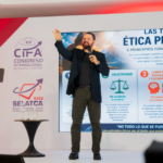 Speaker on stage gesturing with a microphone beside a large presentation about professional ethics.