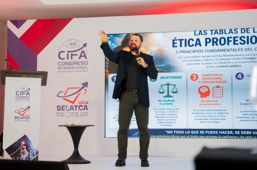 Speaker on stage gesturing with a microphone beside a large presentation about professional ethics.
